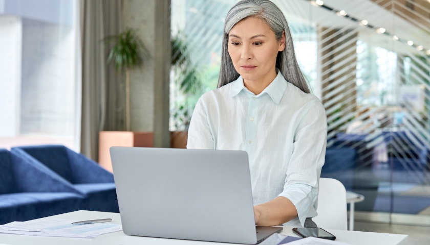 Woman sitting at table, typing on laptop.